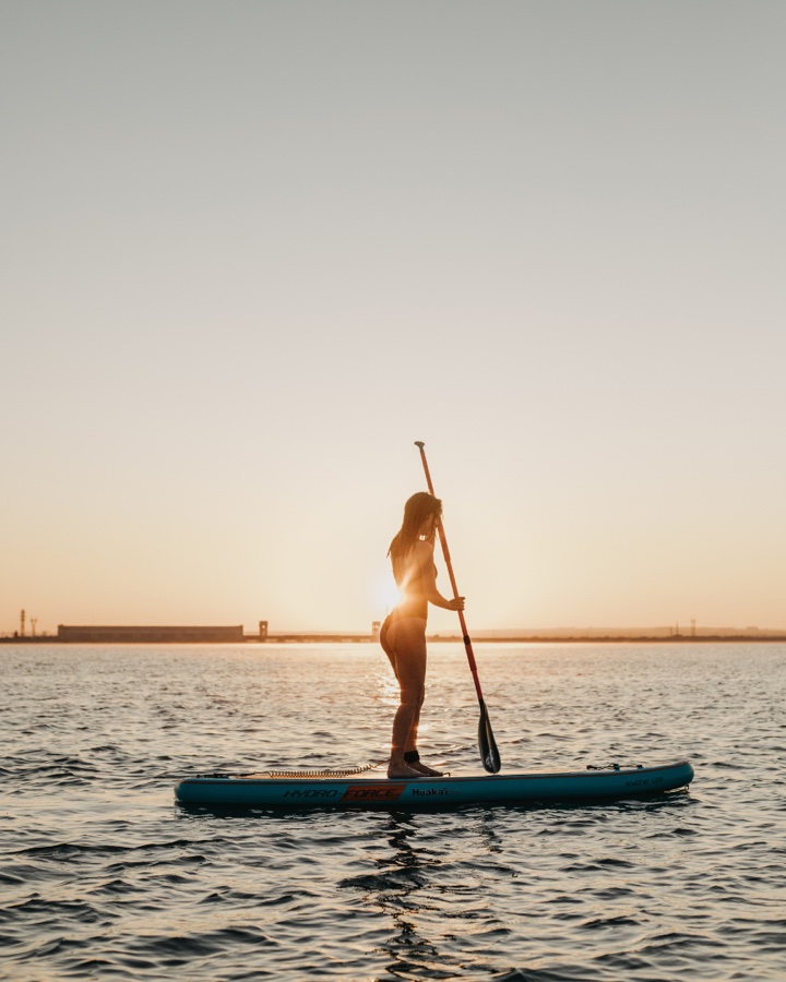 Une personne debout sur une planche de stand up paddle pagaie en mer au coucher du soleil