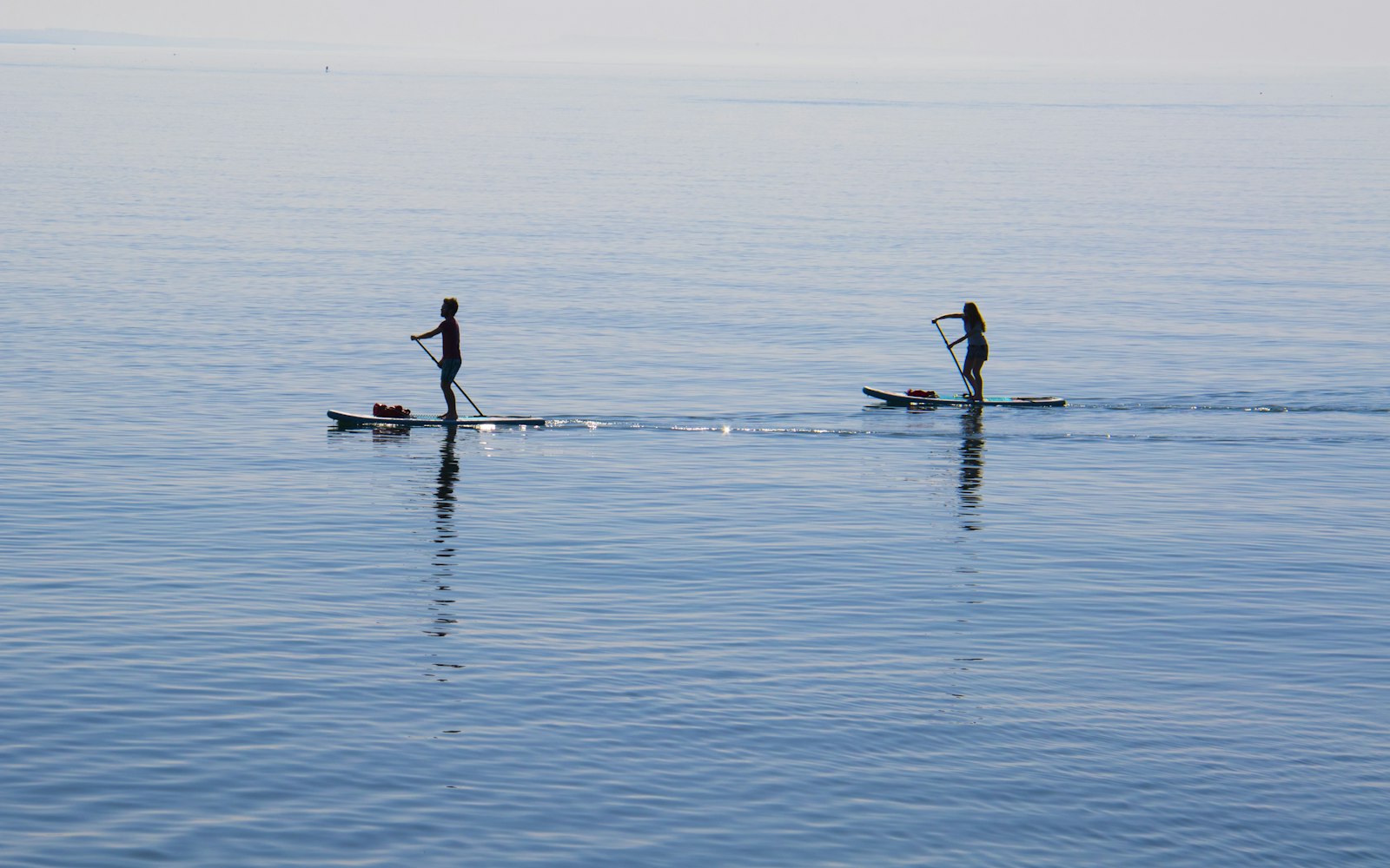 Deux personnes en stand up paddle sur un plan d'eau parfaitement calme