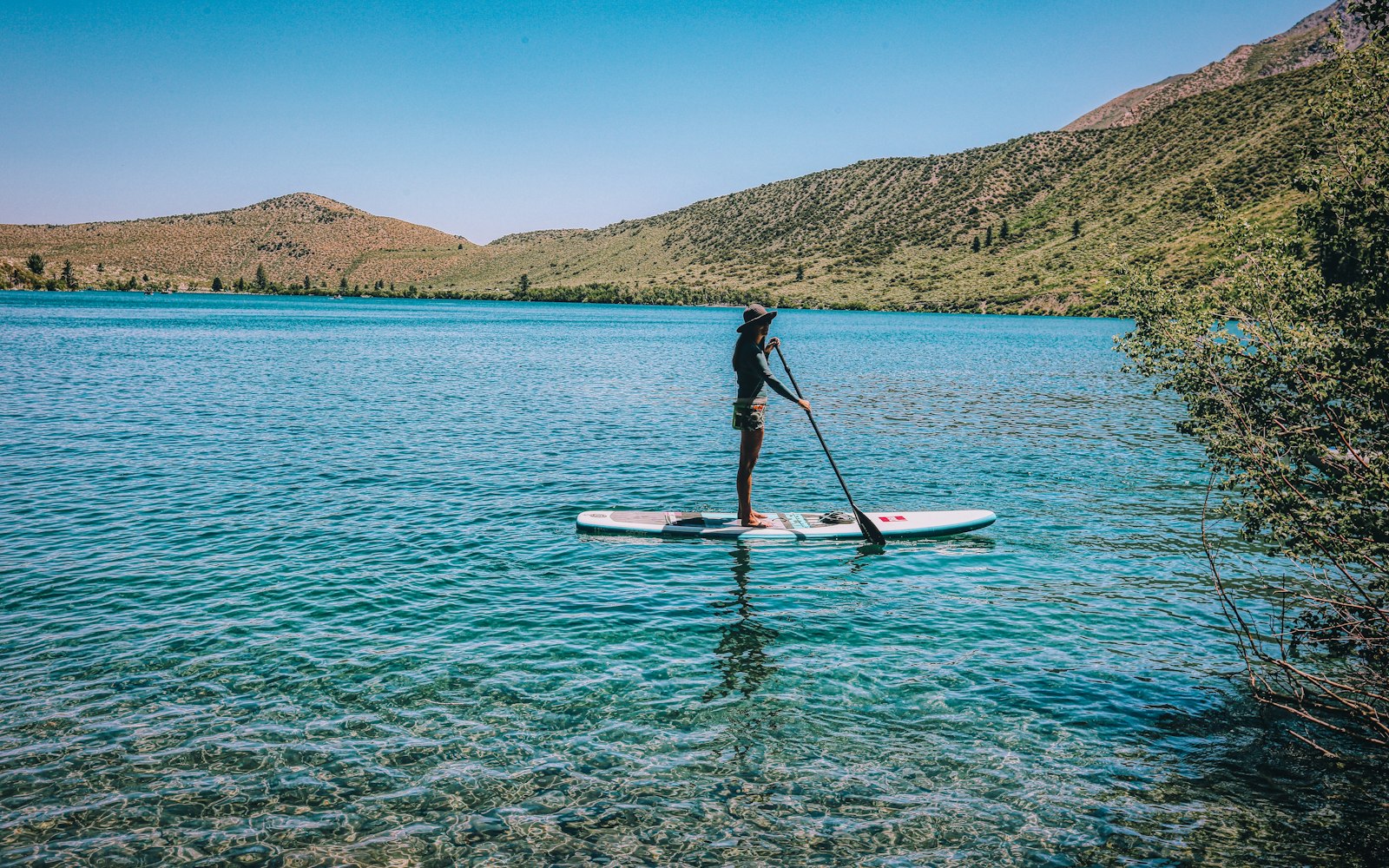Une personne en stand up paddle sur un lac aux eaux turquoise, au pied de collines arides