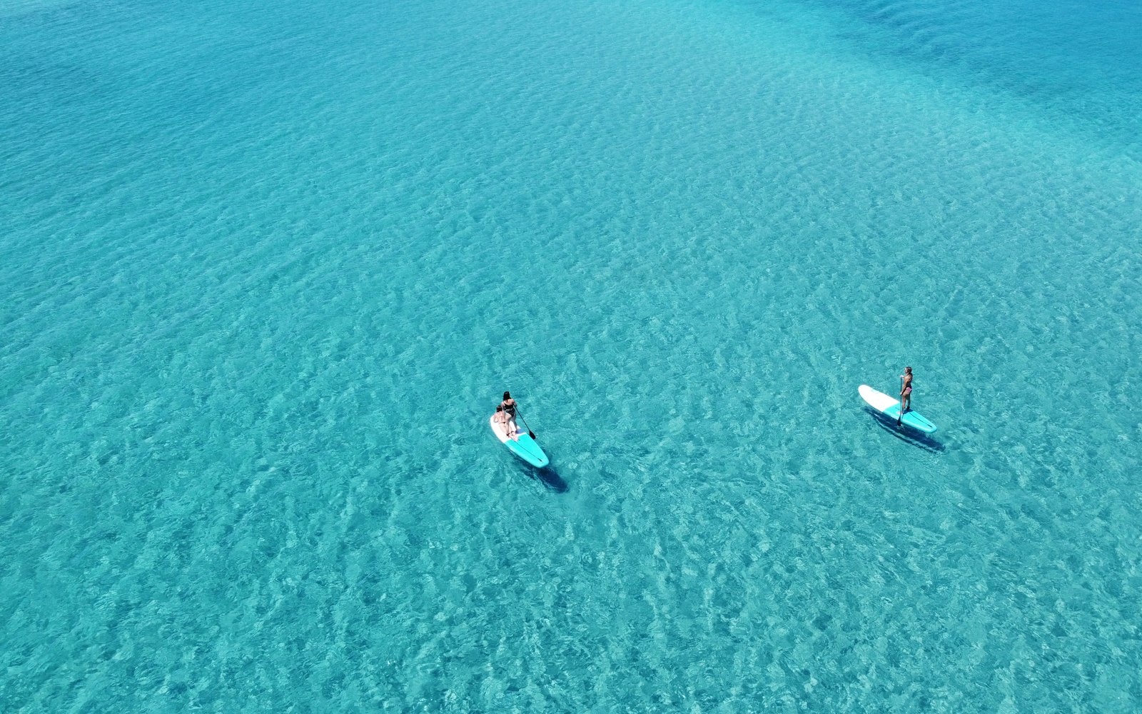 Deux personnes en stand up paddle vues du ciel sur une eau turquoise et transparente