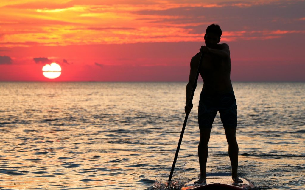 Silhouette d'un pratiquant de stand up paddle devant le soleil couchant sur la mer