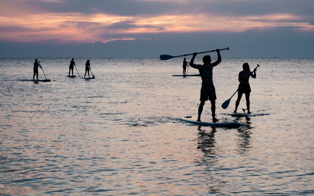 Silhouettes de pratiquants de stand up paddle sur une mer calme au coucher du soleil