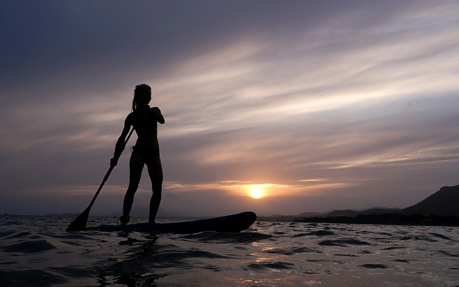 Silhouette d'une personne qui pagaie debout sur son stand up paddle, au coucher du soleil