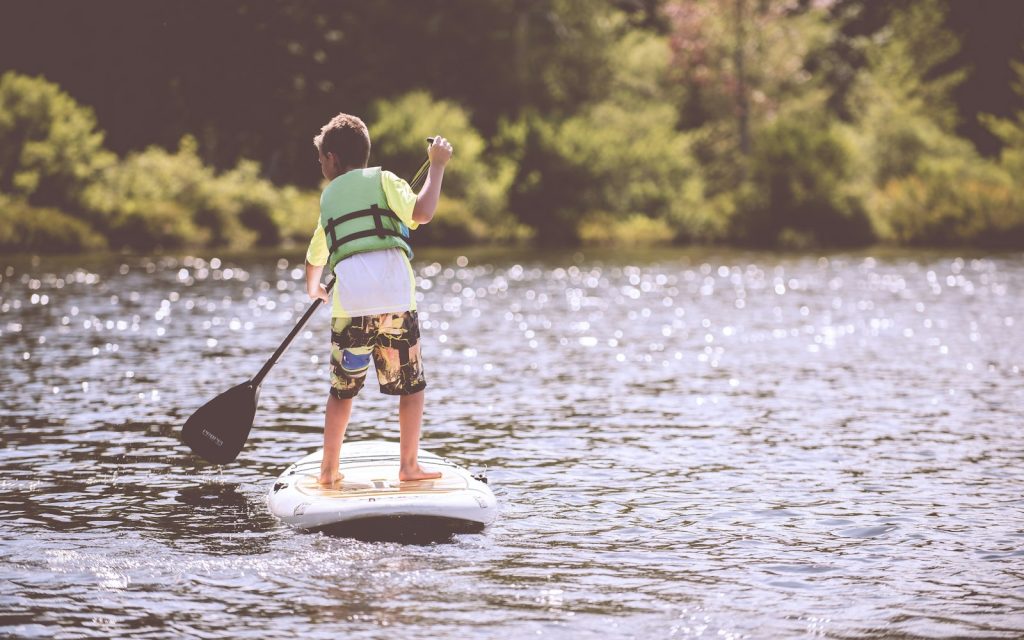 Un enfant en gilet de flottabilité pagaie debout sur une planche de stand up paddle