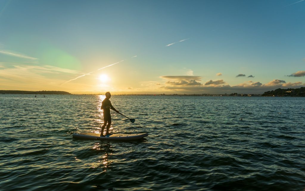 Une personne en stand up paddle sur la mer au lever du soleil