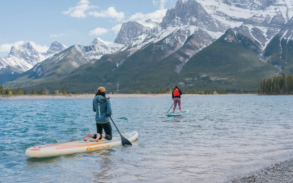 Deux personnes en paddle sur un lac de montagne, face à des sommets enneigés