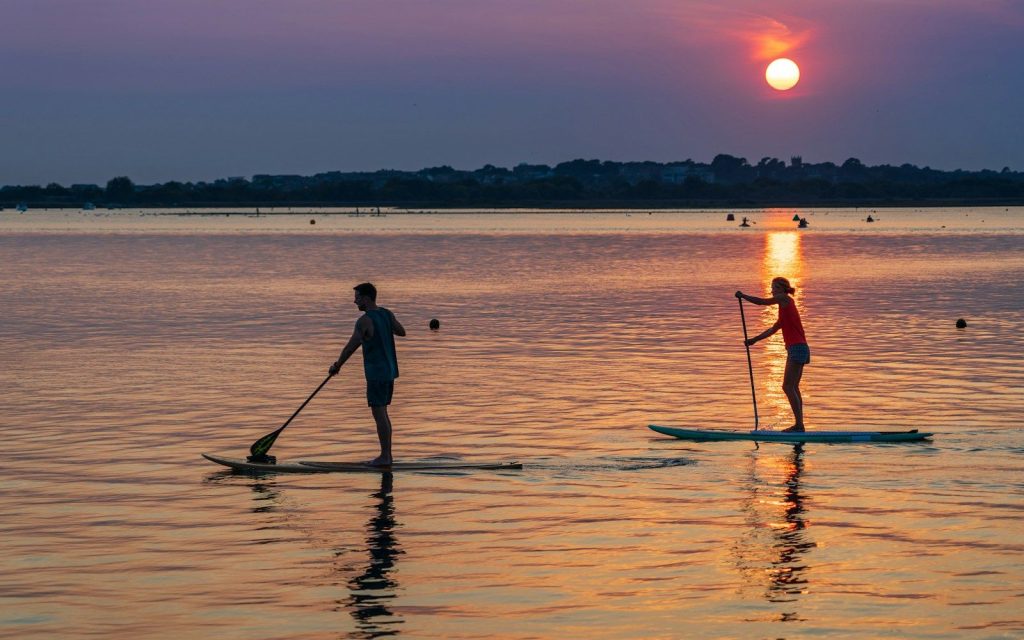 Deux personnes en stand up paddle sur un plan d'eau calme au coucher du soleil