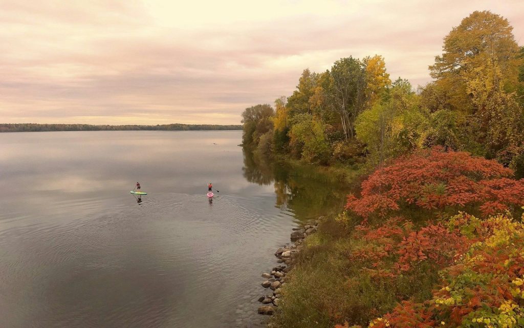 Deux pratiquants de paddle sur une large rivière bordée d'arbres aux couleurs d'automne
